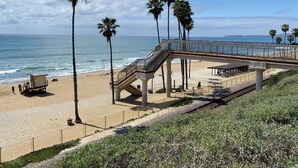 A beach with a lifeguard tower, palm trees, and a pedestrian bridge over the beach.