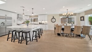 A spacious kitchen with a central island, bar stools, and a dining area with wicker chairs.