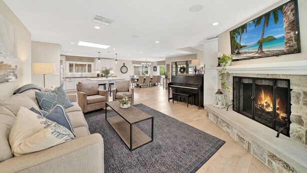 A spacious living room with a fireplace, a dining area, and a kitchen in the background.