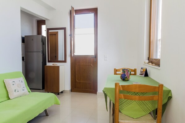 A compact room with a kitchenette, a dining area with a table and chairs, and a green sofa.