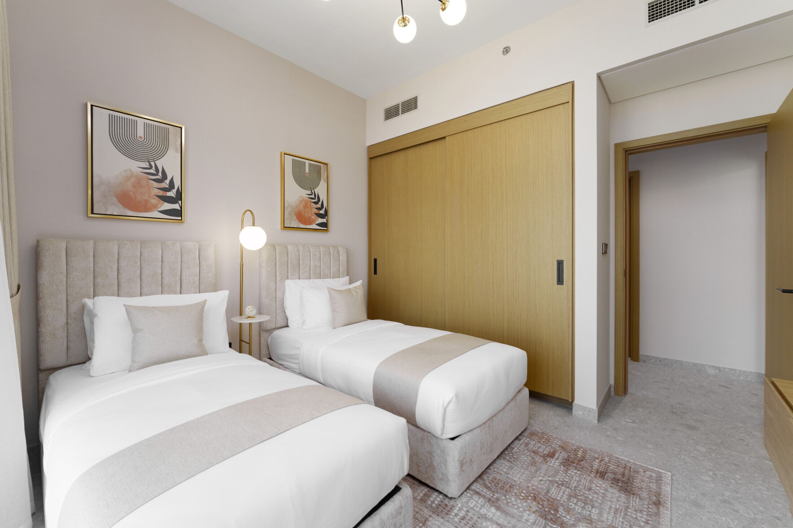 A hotel room with two beds, a wooden wardrobe, and artwork on the walls.