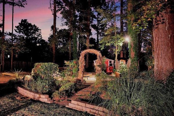 A garden with a brick pathway leading to a red structure, surrounded by trees and plants.
