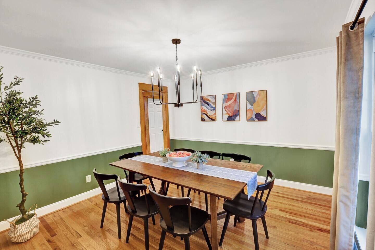 Un comedor con una mesa de madera, sillas negras, una araña y arte abstracto en la pared.