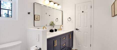 A bathroom with a white toilet, a black vanity with gold handles, a mirror with lights, and a patterned rug.