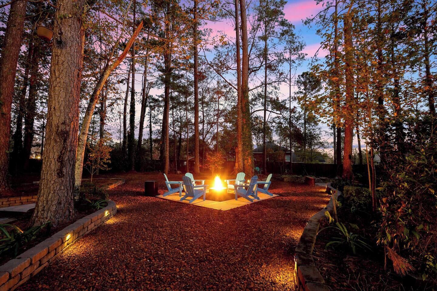 A fire pit with chairs in a forested area at dusk.