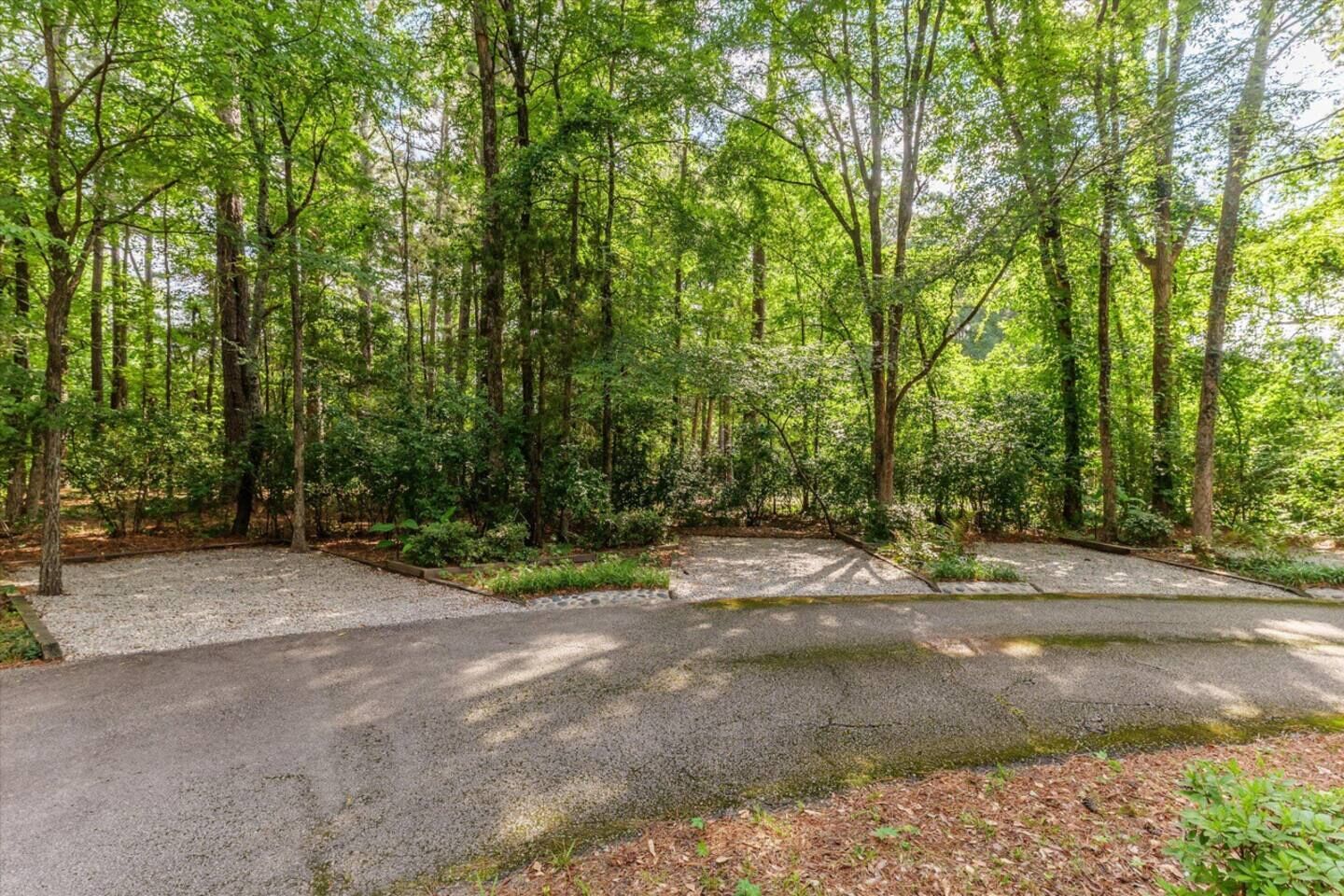 Un terrain de camping doté d’aires de stationnement en gravier et d’un sentier pavé traversant une zone boisée.