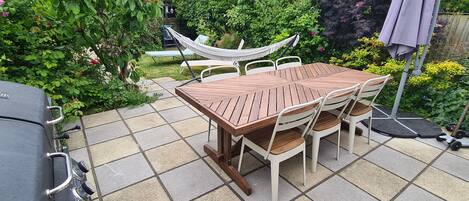 A patio with a wooden table and chairs, a grill, and a hammock.