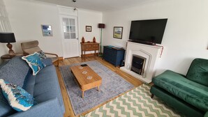 Una sala de estar con un sofá azul, una mesa de centro de madera, un sillón verde, una chimenea y un televisor de pantalla plana.