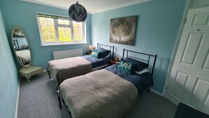 Un dormitorio con dos camas individuales, un aparador, un espejo, una ventana con vistas a árboles y una puerta.