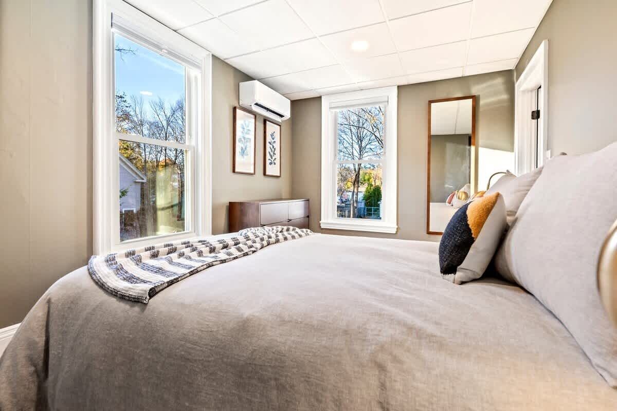 Une chambre à coucher avec un grand lit, une table de chevet, un miroir et deux fenêtres.