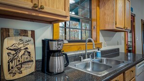 Une cuisine avec des meubles de rangement en bois, une machine à café, un évier et une fenêtre donnant sur les arbres.