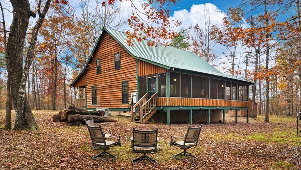 Une cabane en bois avec un toit vert, de grandes fenêtres et une terrasse.