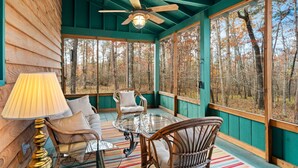 Un chalet confortable avec un intérieur en bois, un ventilateur de plafond, une table en verre, des chaises en osier et une vue sur la forêt grâce à de grandes fenêtres.