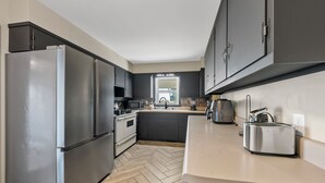 Een moderne keuken met een roestvrijstalen koelkast, donkere kastjes, een visgraat houten vloer en een broodrooster op het aanrecht.