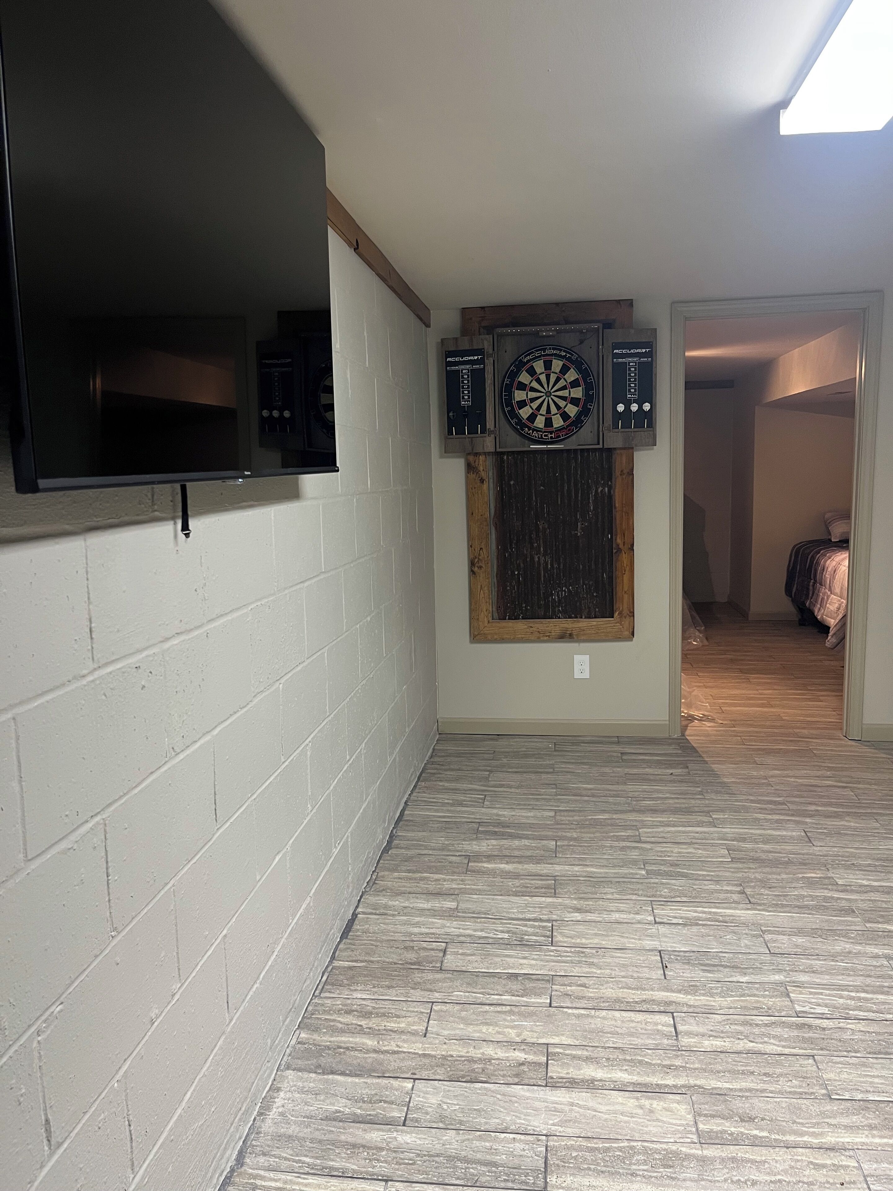A room with a flat-screen TV mounted on a brick wall, a dartboard, and dartboards on the wall.