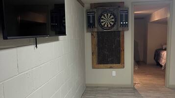A room with a flat-screen TV mounted on a brick wall, a dartboard, and dartboards on the wall.