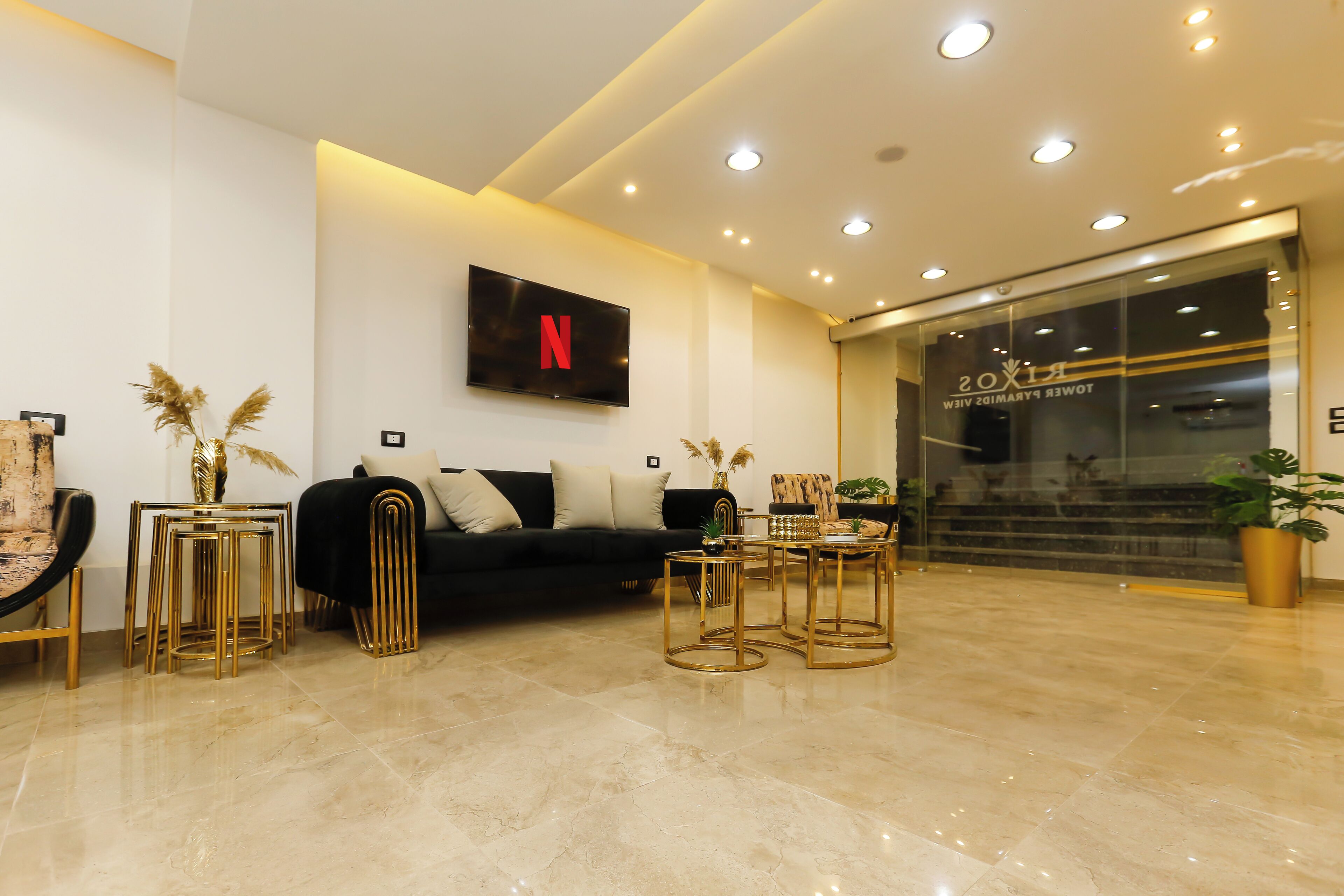 Un vestíbulo moderno con un sofá negro, mobiliario dorado y una televisión que muestra el logotipo de Netflix.
