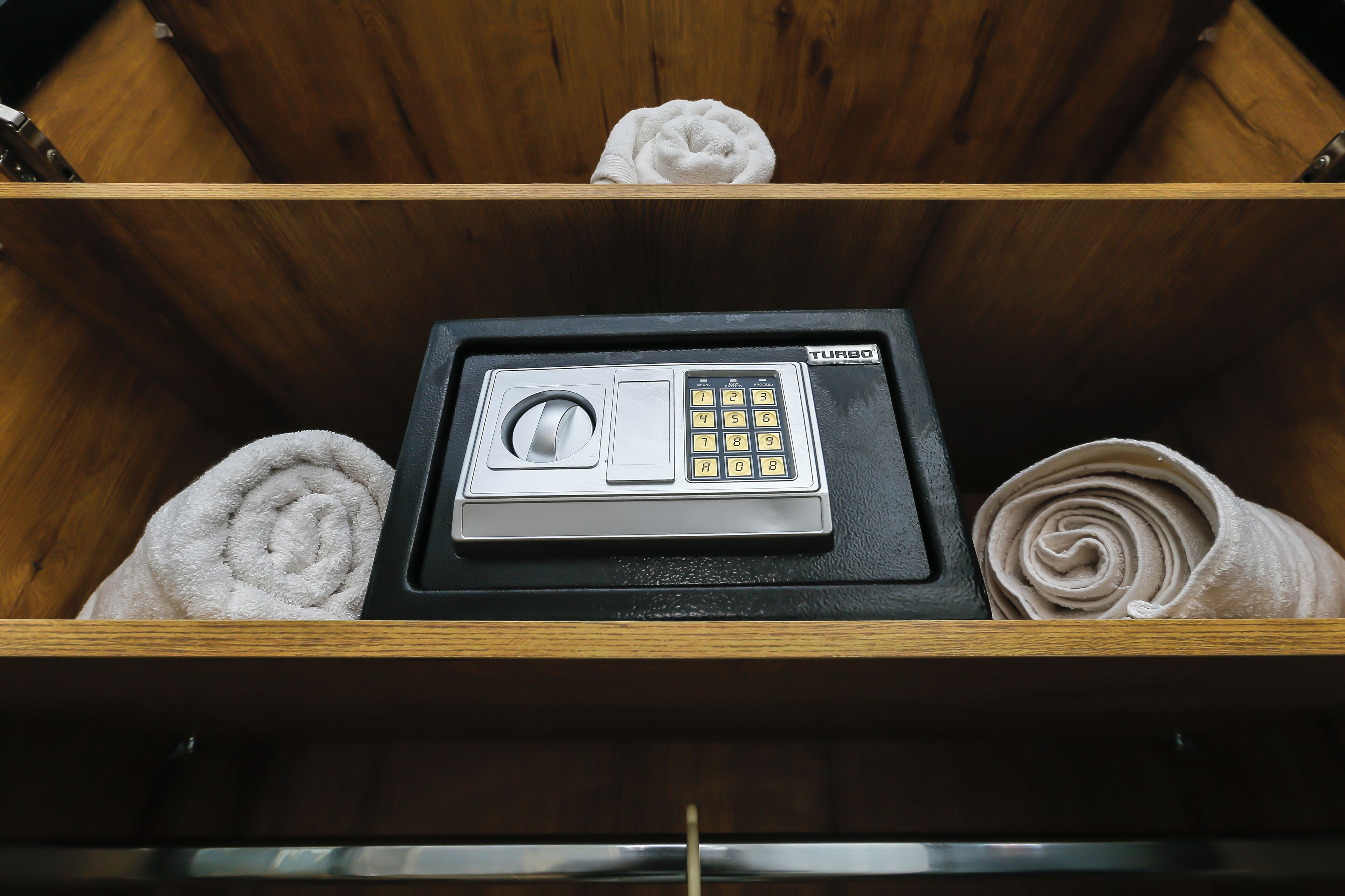 A wooden drawer with a black electronic device, possibly a safe, and two rolled towels.