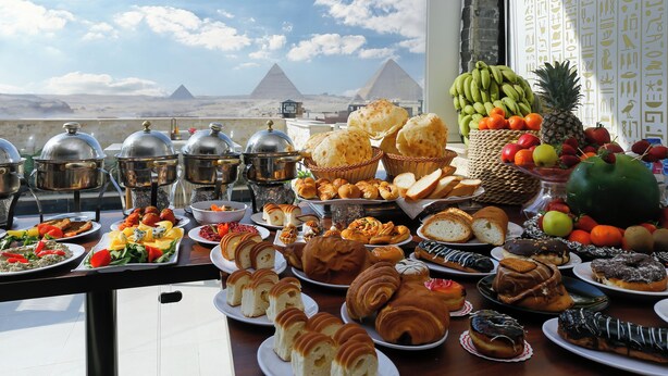 Ein reichhaltiges Buffet mit verschiedenen Speisen und Blick auf die Pyramiden im Hintergrund.