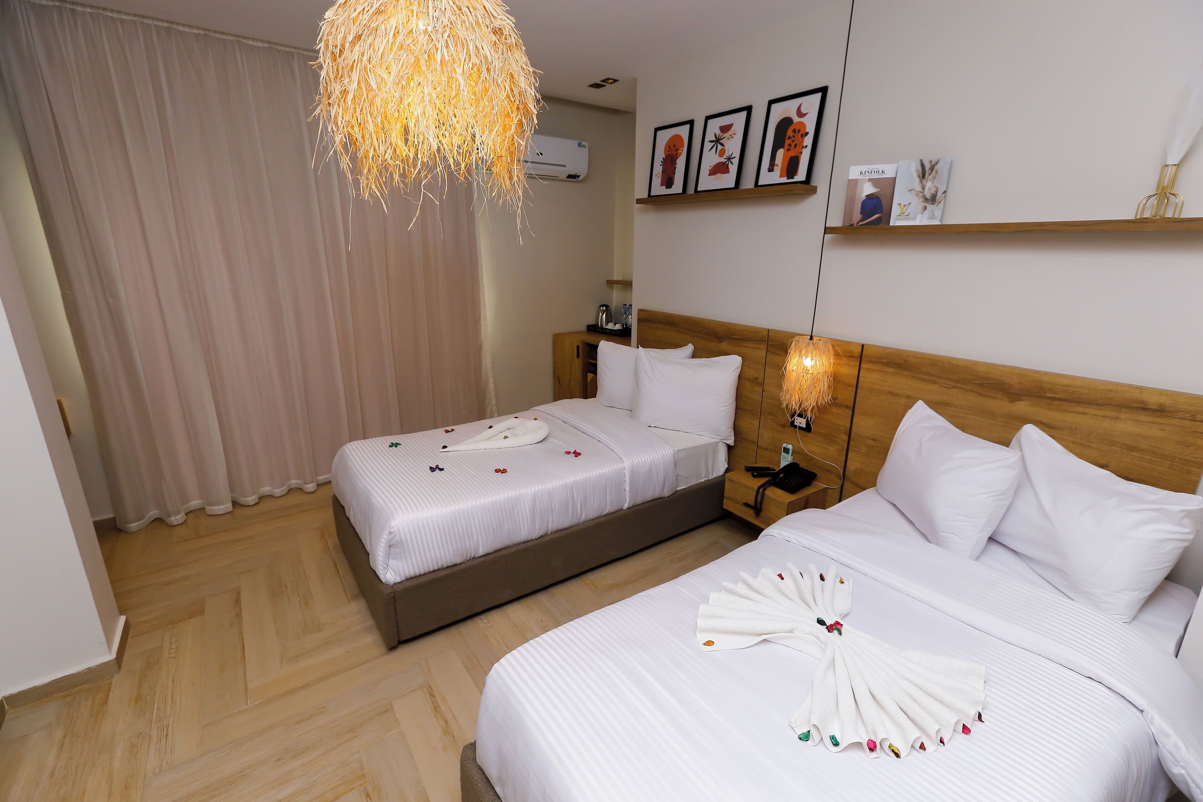Ein Hotelzimmer mit zwei Betten, einem hölzernen Kopfteil, einer Pendelleuchte und einer Wand-Klimaanlage.