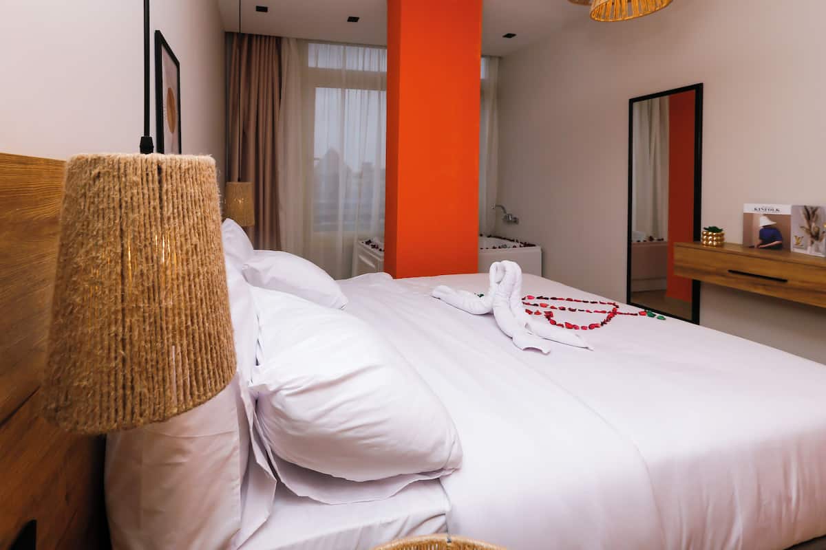A neatly made bed with white linens, a woven headboard, and a red accent wall.