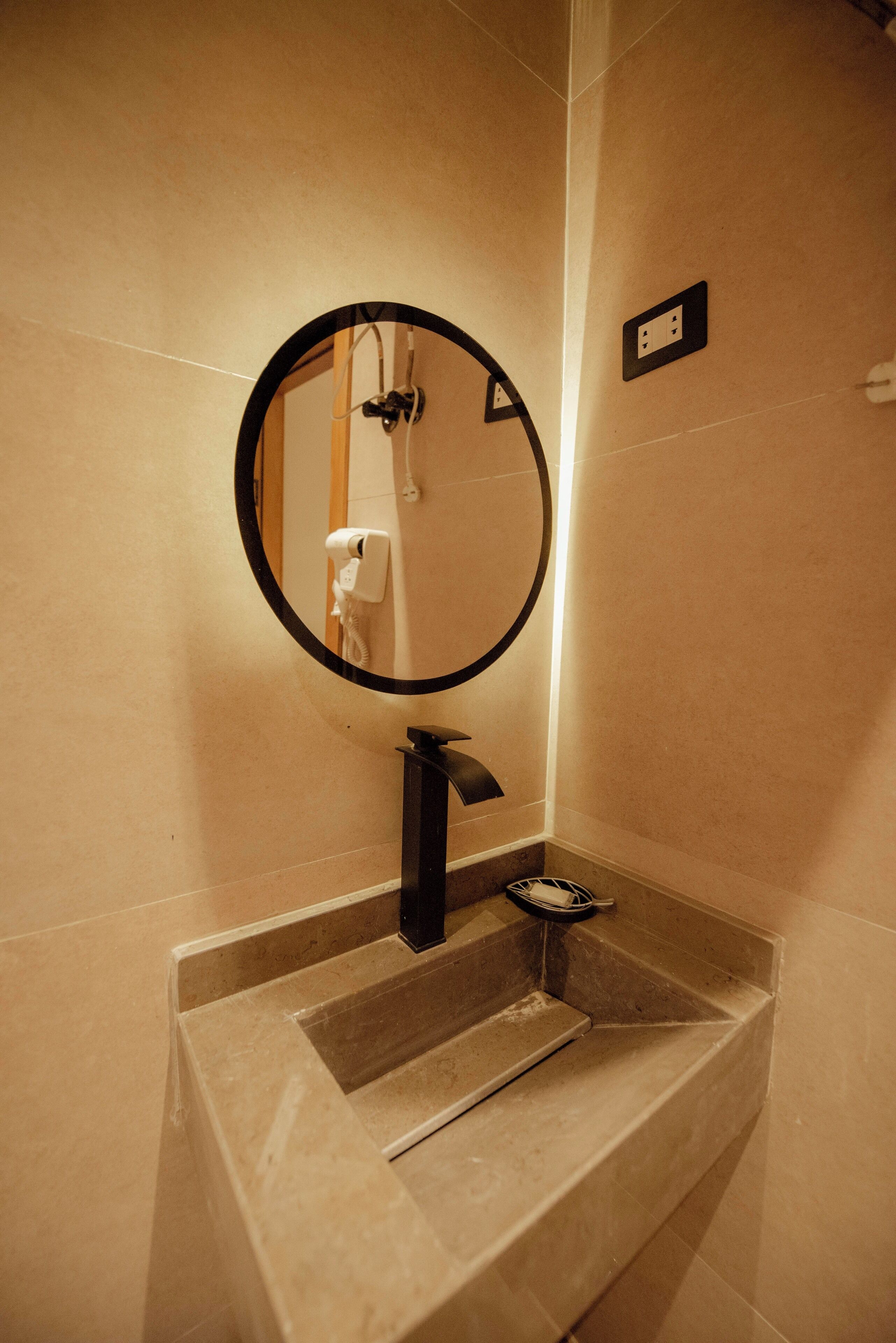 A bathroom with a round mirror, a sink, and a hairdryer.