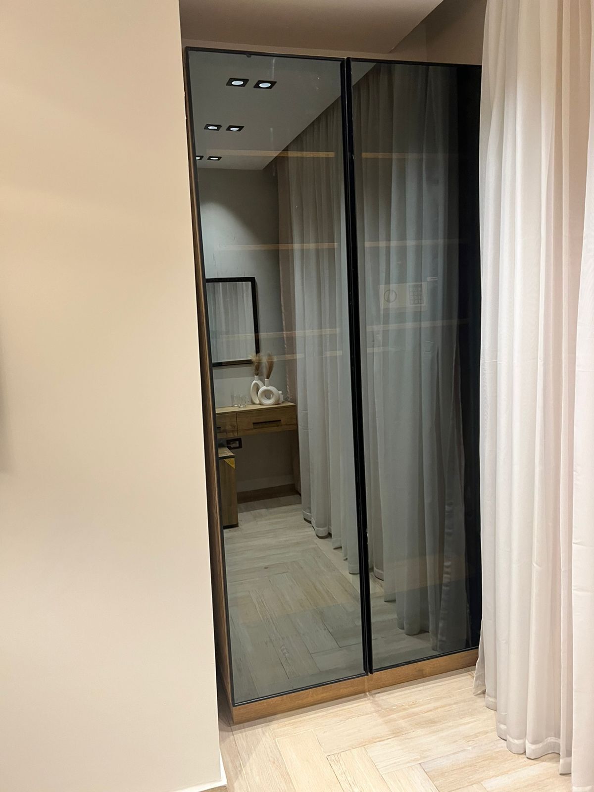 A modern bathroom with a glass partition, wooden floor, and a mirror above the sink.
