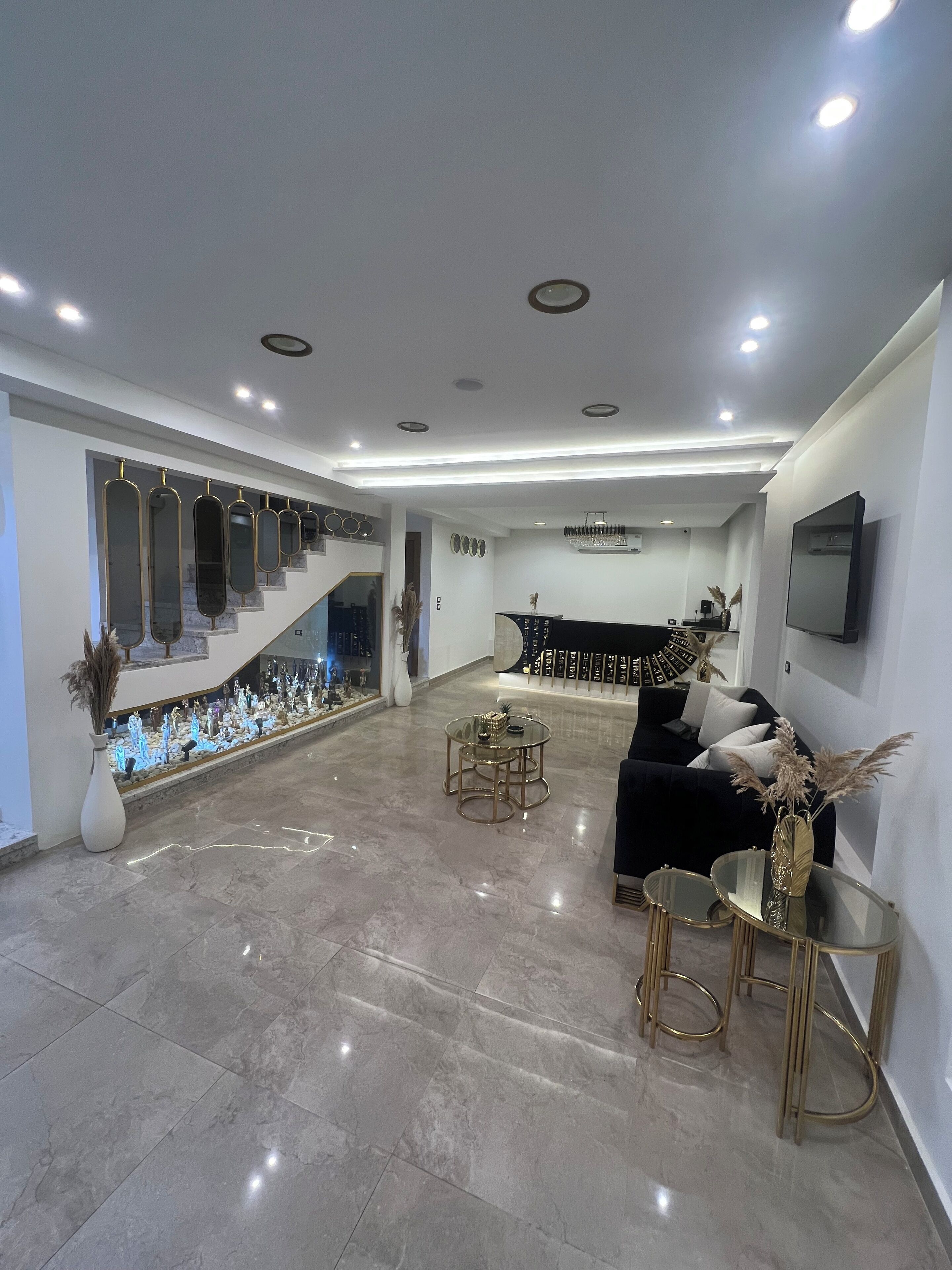 A spacious living area with a staircase, a black sofa, a round glass table, and a flat-screen TV mounted on the wall.
