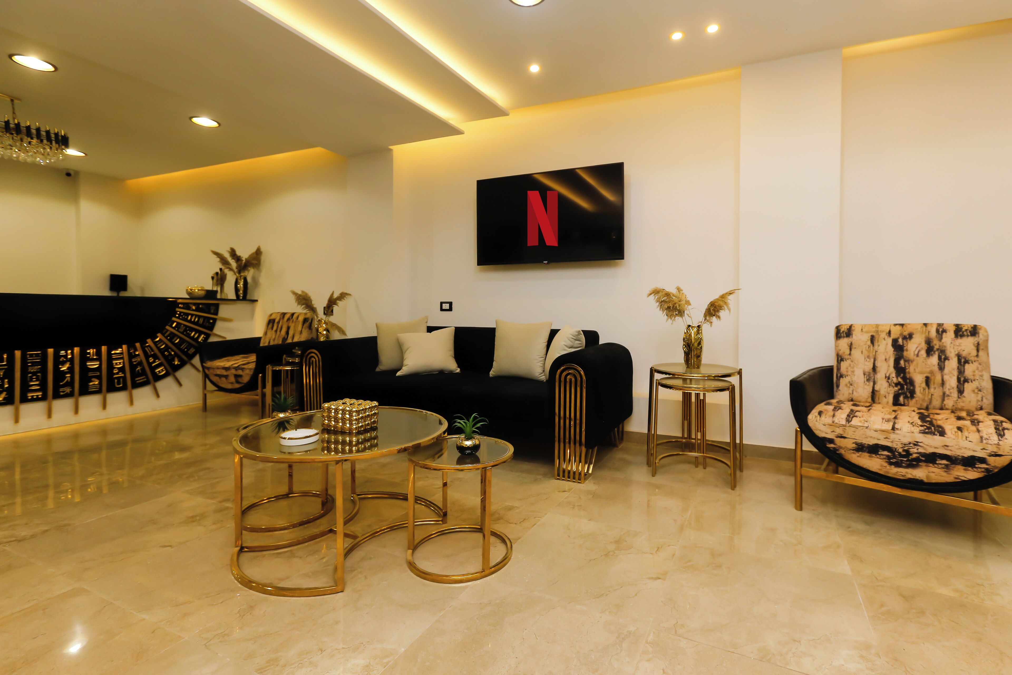 A modern living room with a black sofa, a gold-framed coffee table, and a TV mounted on the wall displaying the Netflix logo.