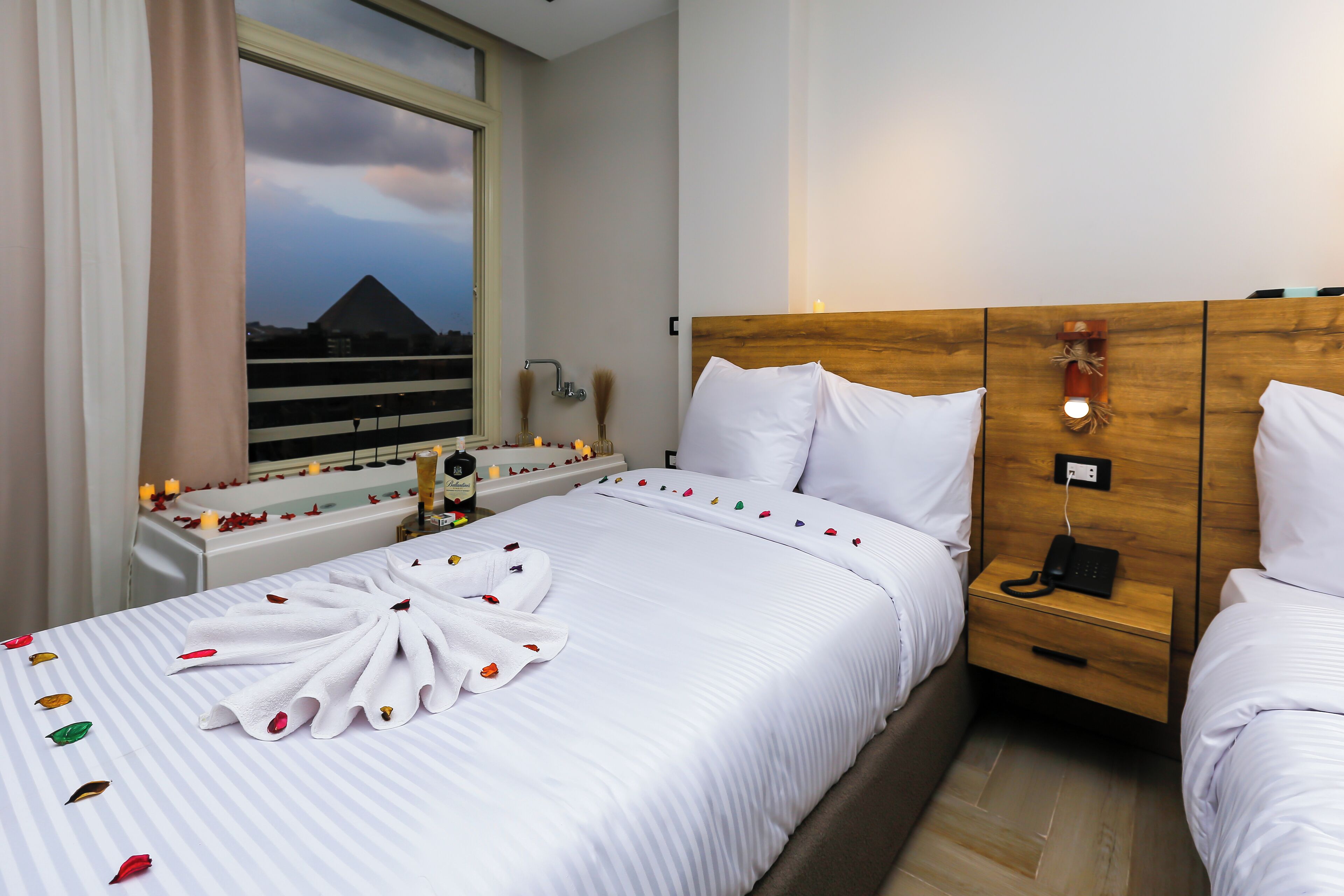 A hotel room with a bed, bedside table, and a view of a pyramid through a window.