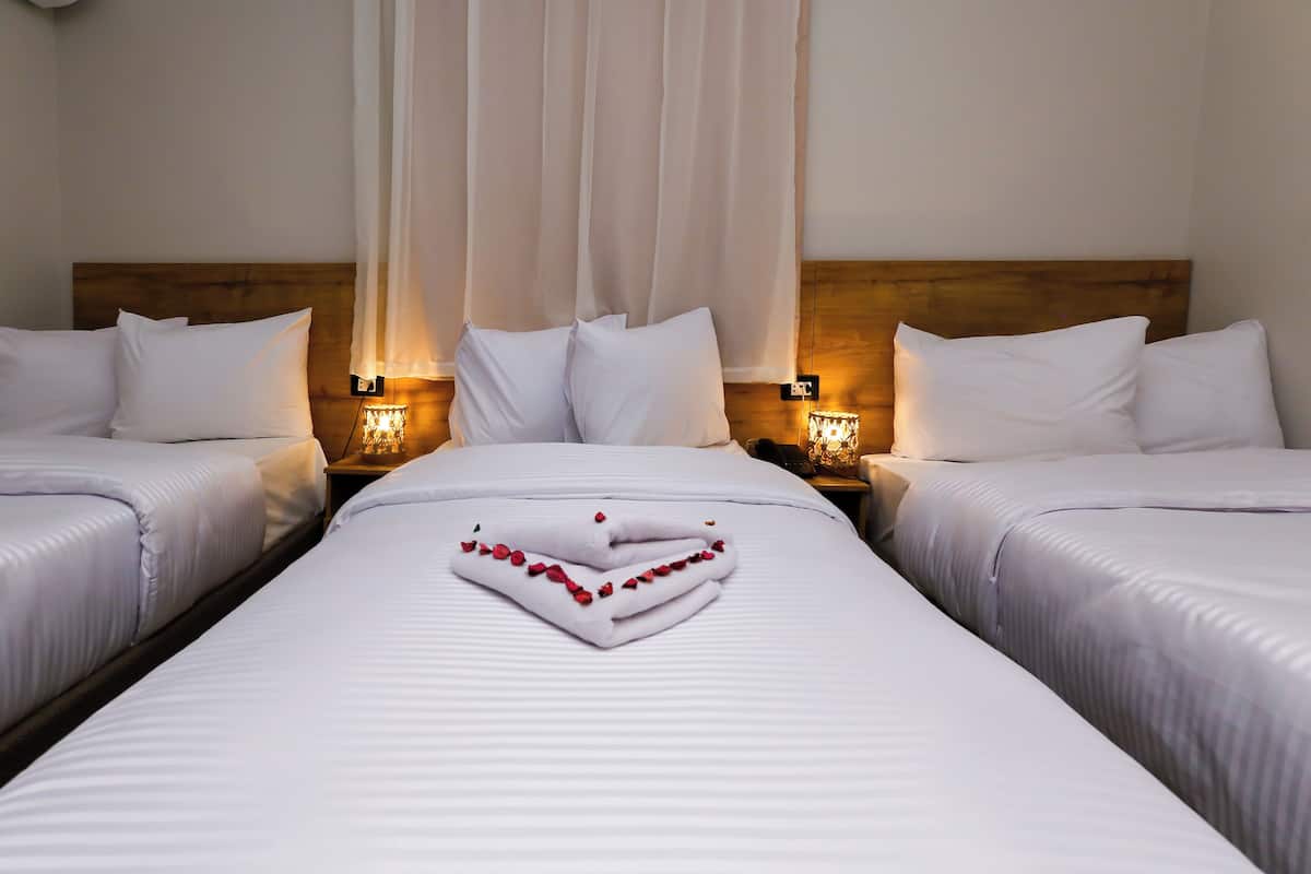 A hotel room with two beds, white linens, and a heart-shaped towel decoration.