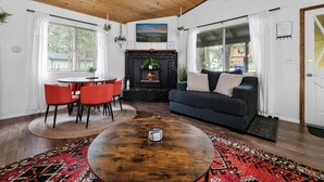 Una sala de estar acogedora con chimenea, una mesa de centro redonda, un sofá y un comedor con sillas rojas.