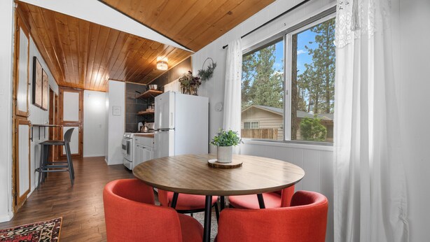 Una cocina con techo de madera, una mesa de comedor con cuatro sillas rojas y una ventana con cortinas blancas.