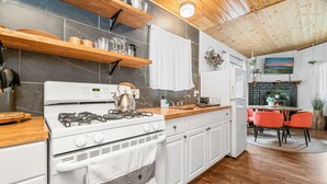 Una cocina moderna con estufa a gas, armarios blancos y encimeras de madera. Hay un comedor con mesa y sillas.