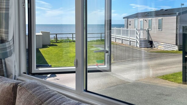 A view from a window overlooking a grassy area with a wooden deck and a building with a sloped roof. - 3 bedroom accommodation in Lancaster (Lancaster)