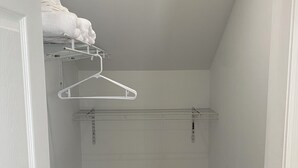 Ein schmaler Korridor mit Holzboden, weißen Wänden und einem weißen Schrank mit Kleiderstange und Regalen.