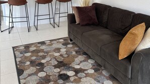 Ein modernes Wohnzimmer mit einem braunen Sofa, einem gemusterten Teppich und einer Küche im Hintergrund.