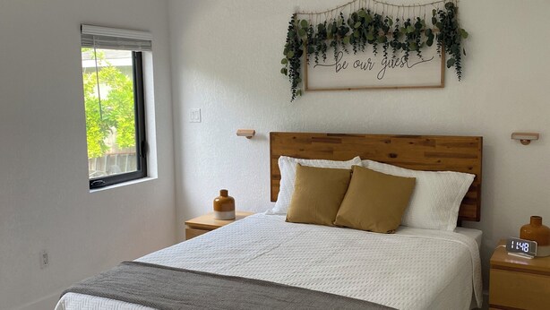 Ein Schlafzimmer mit einem Bett, einem Deckenventilator, einer Wandpflanze und einem Nachttisch mit einer Uhr.