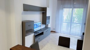 Sala de estar moderna com televisão de tela plana, armários cinzas, mesa de madeira e varanda com vista.