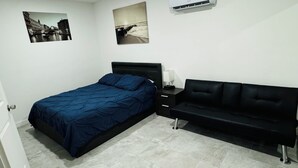 Una camera da letto con un letto, un divano nero, un comodino e due quadri appesi al muro.