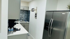 Una cucina compatta con frigorifero in acciaio inossidabile, un piano di lavoro bianco e una parete attrezzata con motivo effetto pietra.