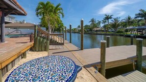 Un muelle de madera con una tumbona de mosaicos, palmeras y una masa de agua tranquila.