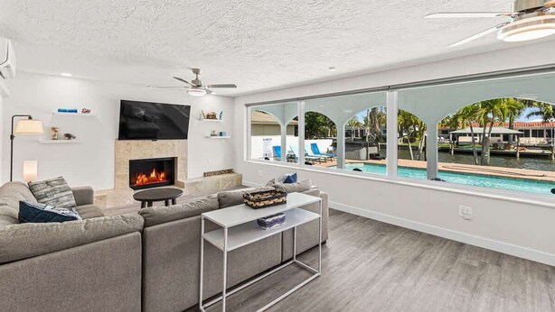 Una sala de estar moderna con chimenea, televisor grande y vista a una piscina.