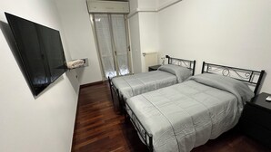 Een slaapkamer met twee bedden, een aan de muur bevestigde televisie, een raam met gordijnen en een radiator.