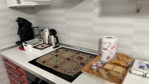 Een keuken met een koffiezetapparaat, een waterkoker, een pak keukenpapier en een schaal met brood en gebak.