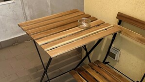 Een houten tafel met een glazen vaas erop, geplaatst tegen een muur met een raam en een betegelde vloer.