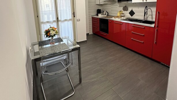 Een kleine keuken met een eethoek, met een glazen tafel, een rode koelkast en een magnetron.