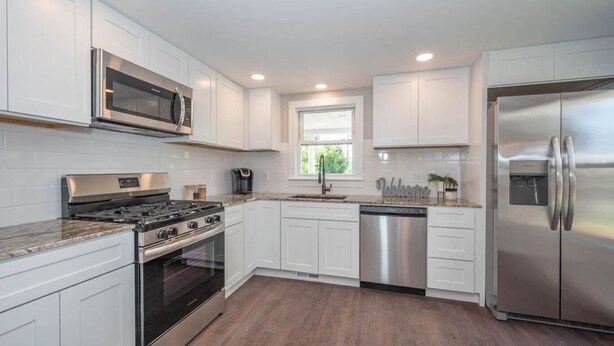 A modern kitchen with white cabinets, stainless steel appliances, and a wooden floor. - Beautiful 3 Bedroom Downtown Salem Home (Salem)