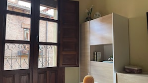 Une pièce avec une porte en bois, une fenêtre avec des barreaux en métal, une table en bois et une étagère contenant des livres et des objets décoratifs.