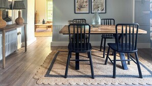 A dining area with a wooden table, black chairs, a woven rug, and two framed artworks on the wall. - 2 bedroom accommodation in Bodmin (Bodmin)